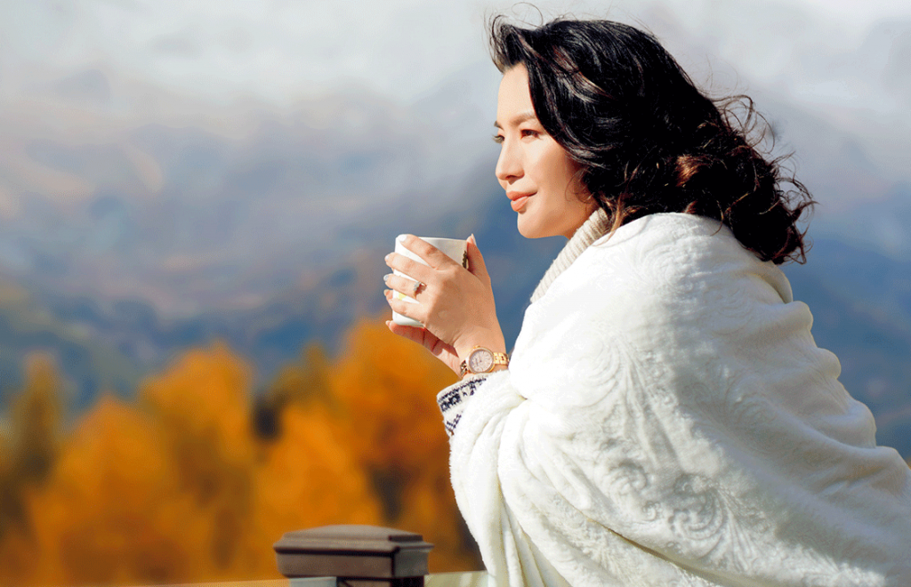 women holding mug looking out, mountains and fall trees in background